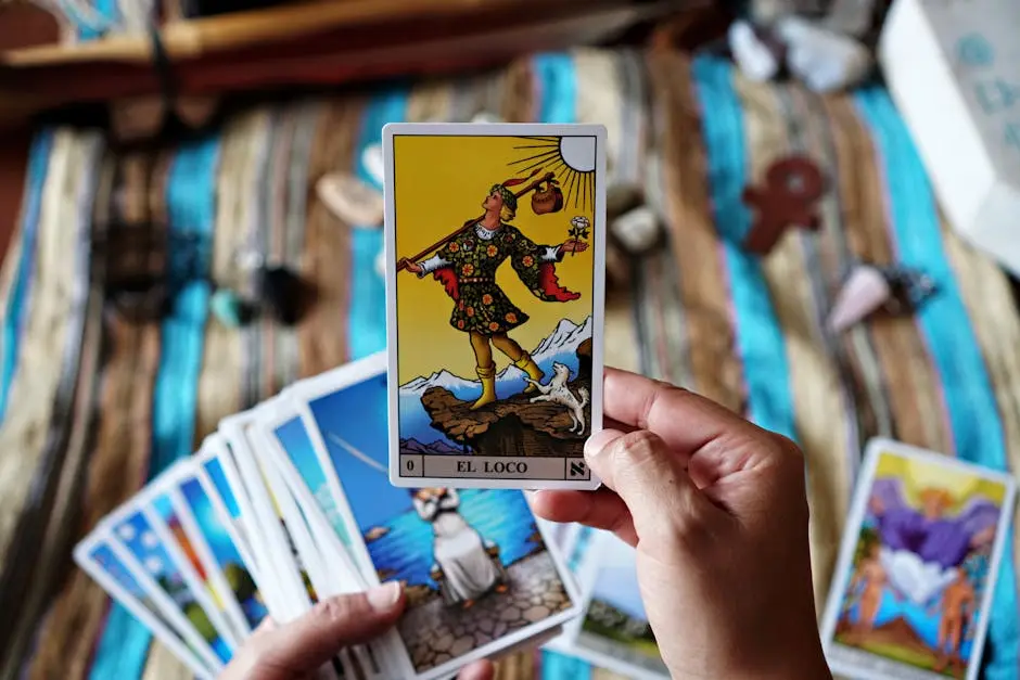 A person holds a tarot card ‘El Loco’ with a background of more cards, symbolizing fortune telling.