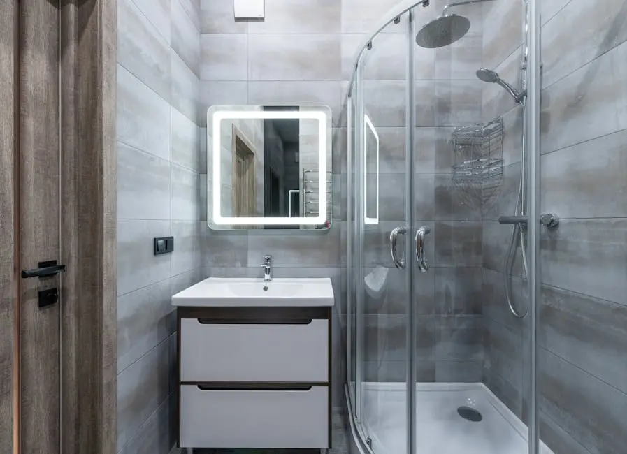 Contemporary washbasin under mirror against shower room with glass walls and tiles at home