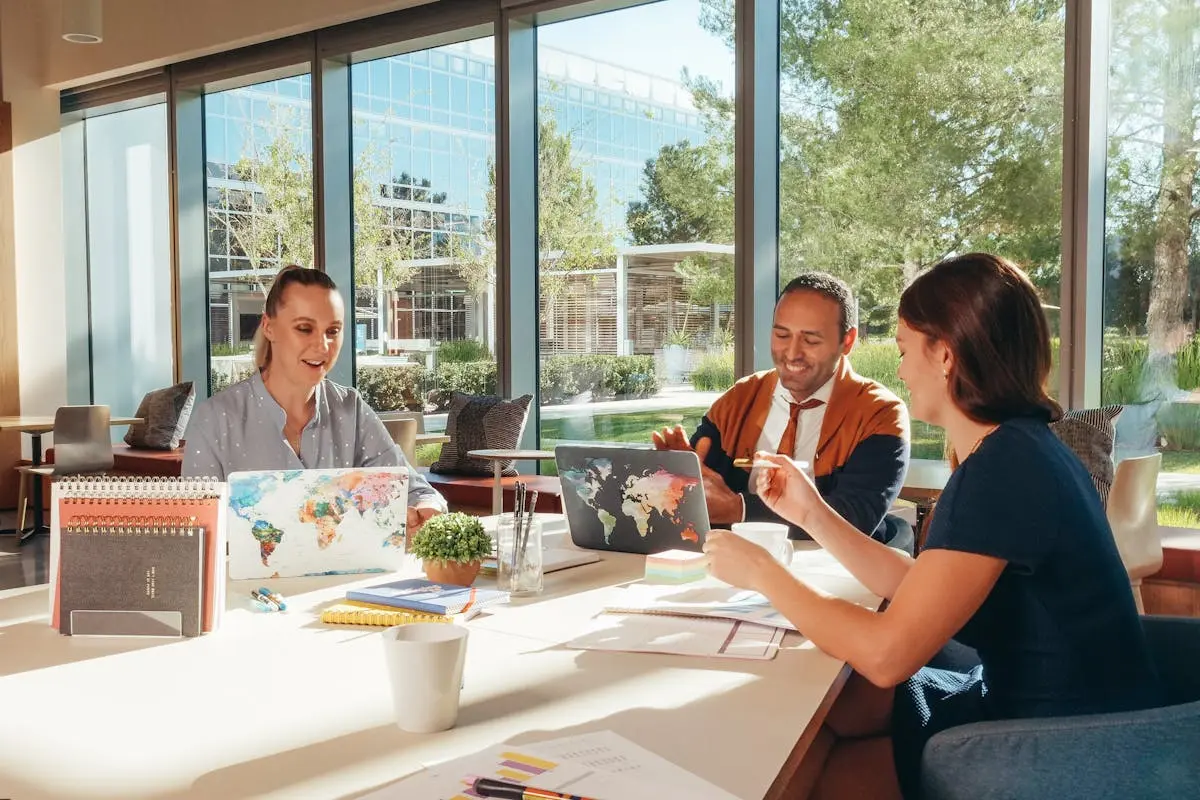 Three colleagues brainstorming with laptops in a well-lit office.