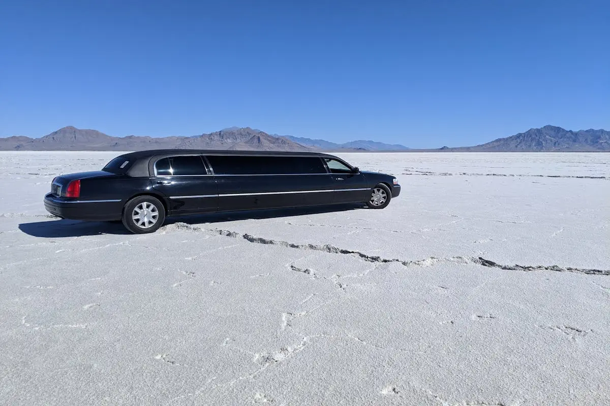 A sleek black limousine parked in a vast, dry desert with a clear blue sky.
