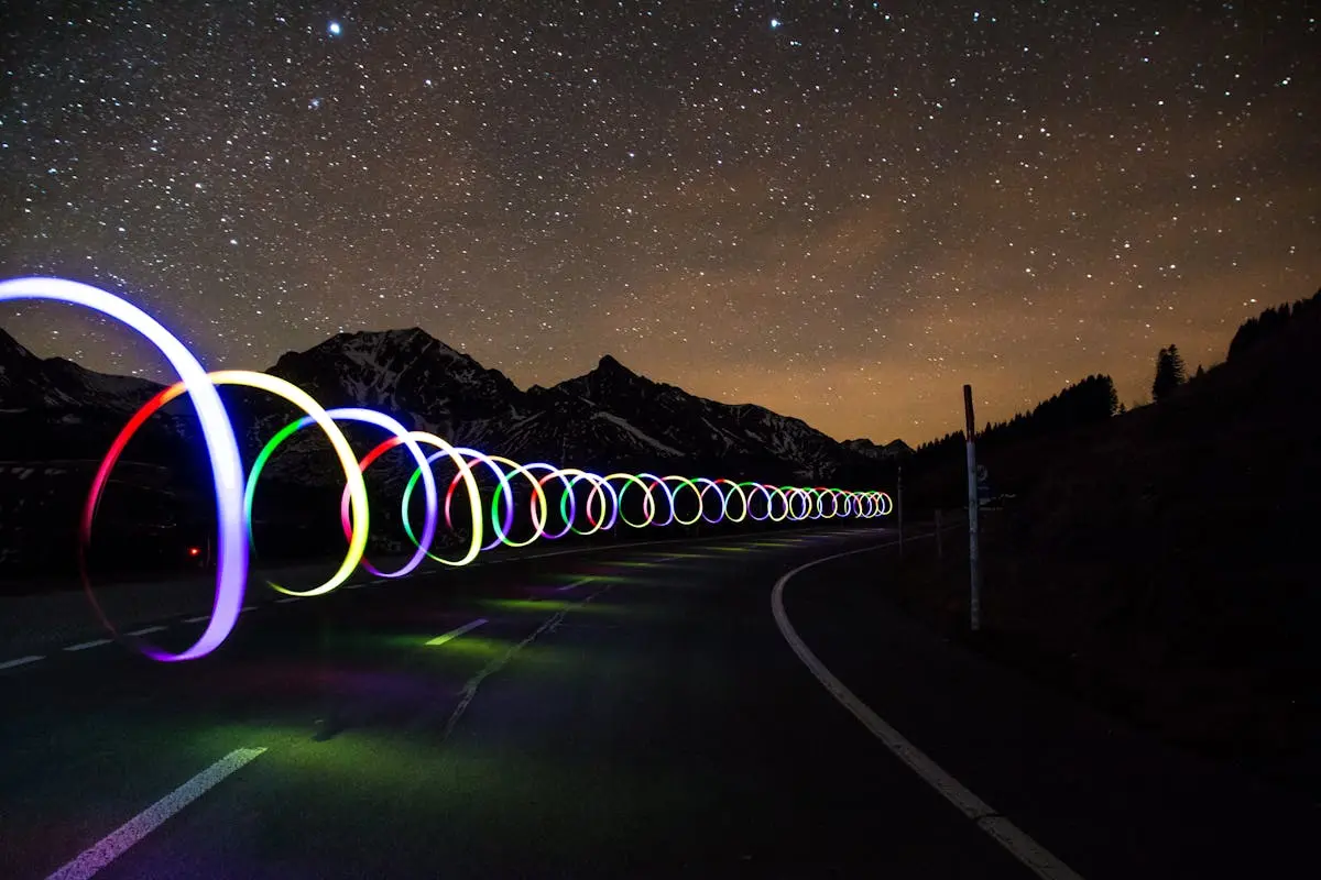 Enchanting long exposure of colorful light trails on a winding road beneath a star-filled sky.