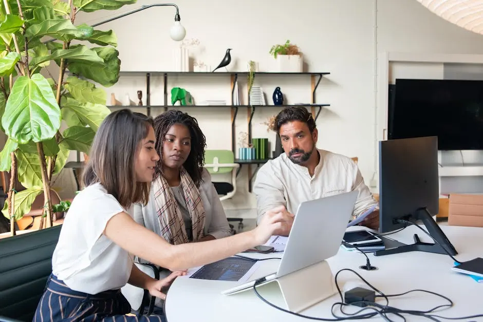 A diverse group of professionals collaborating in a modern office setting, working on laptops around a table.