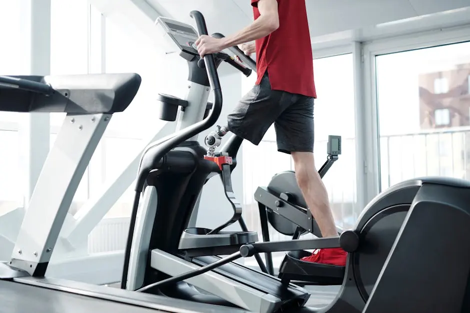 Adult man in gym exercising on an elliptical trainer, focusing on fitness and endurance indoors.