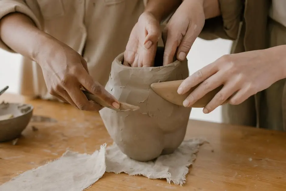 Hands shaping clay pottery collaboratively, showing craftsmanship.