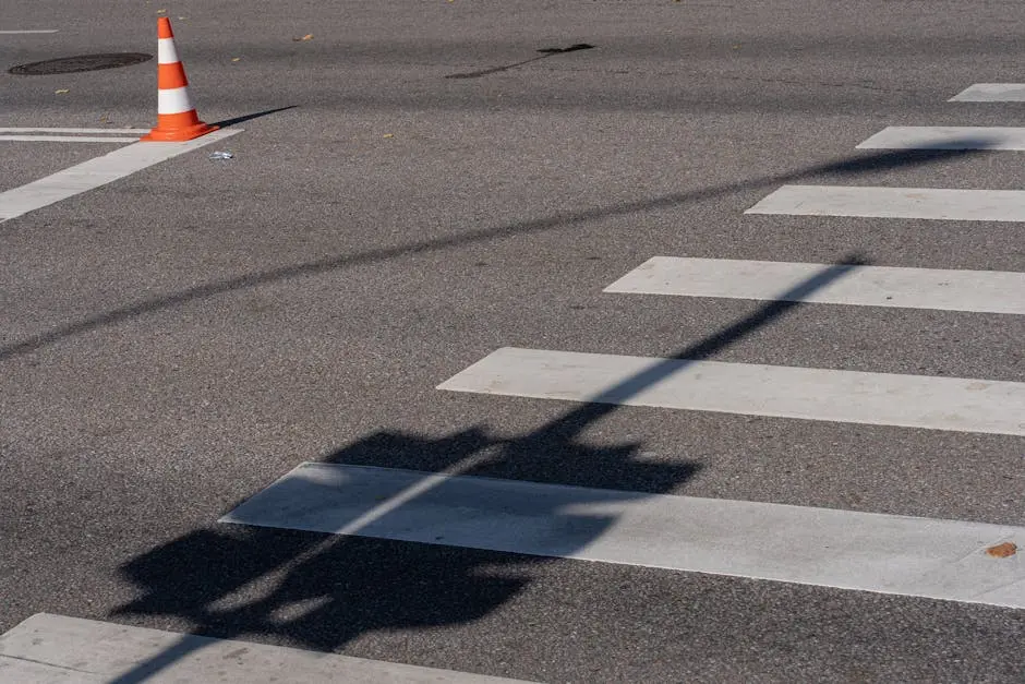 Street scene with a traffic cone, crosswalk, and shadows, capturing urban infrastructure.