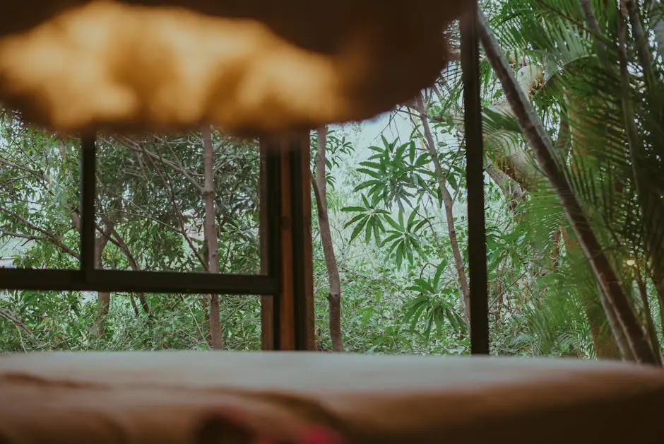 Inviting tropical room interior with greenery outside a large window, perfect for relaxation.
