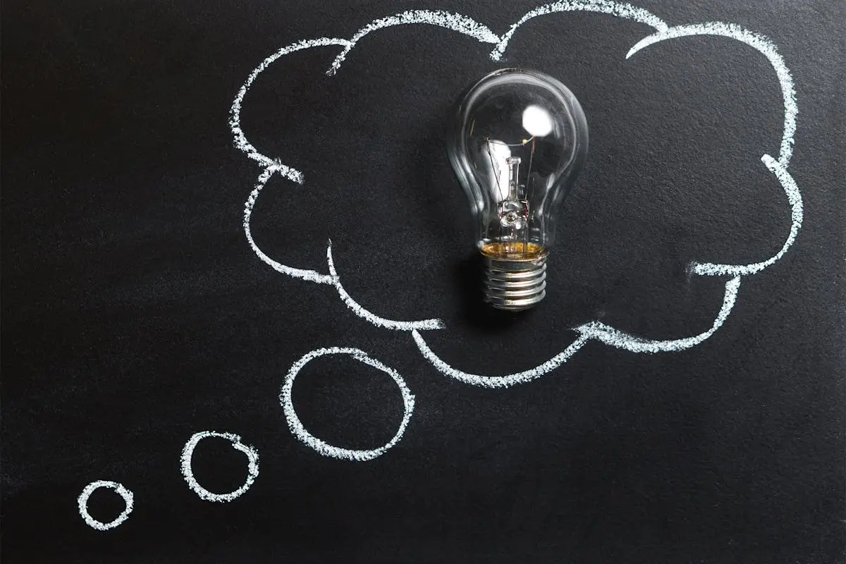 Light bulb laying on chalkboard with drawn thought bubble, symbolizing creative ideas.