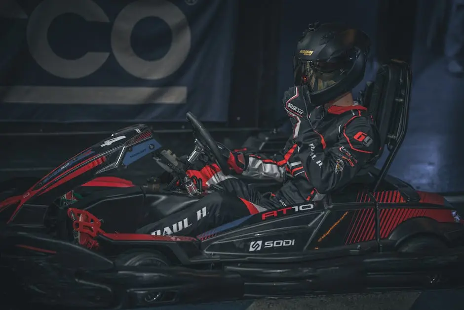 A go-kart racer in full gear on an indoor track, ready to start racing.