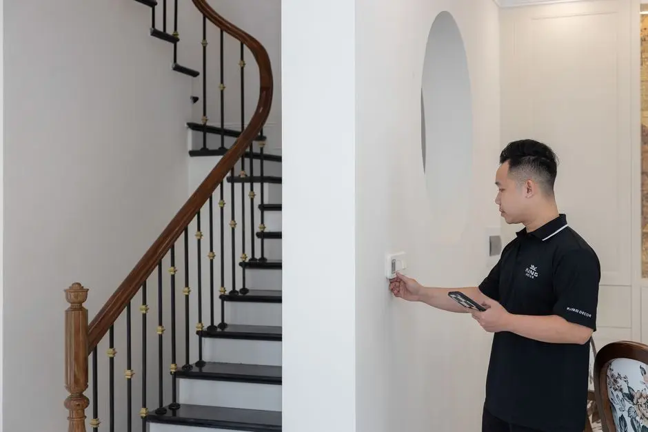Man adjusting thermostat in stylish home with elegant staircase.
