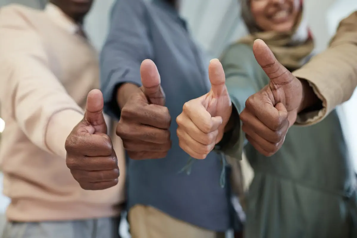 Close-up of a it consulting team giving thumbs up indoors, symbolizing success and unity.