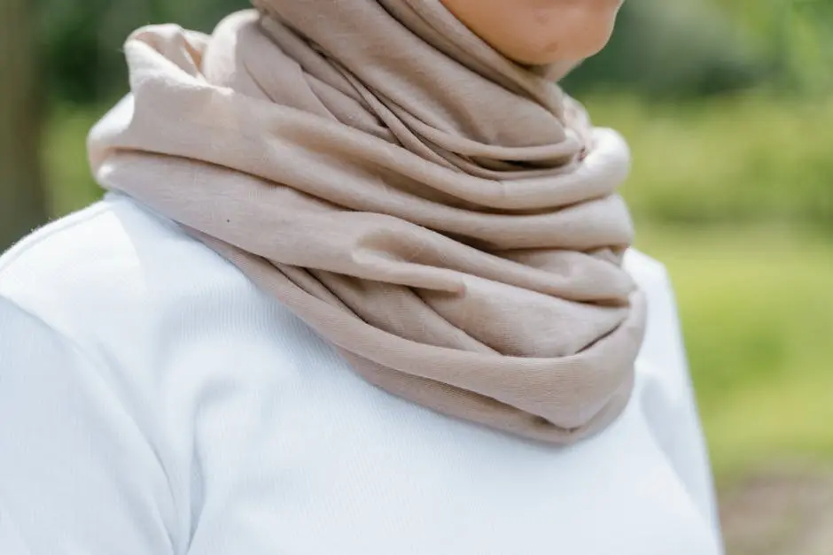 A stylish beige scarf draped around a white sweater, captured in an outdoor setting.