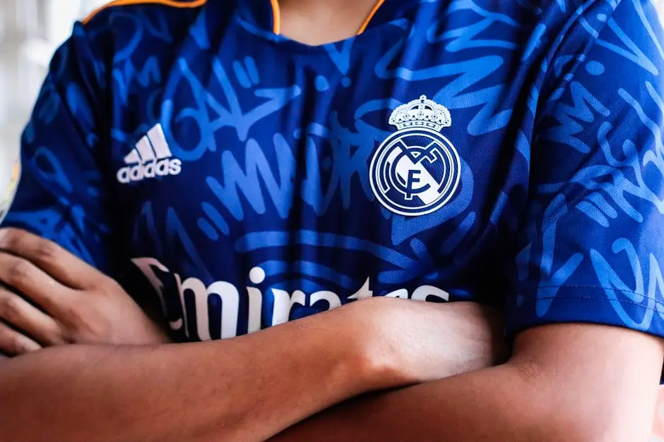 Arms crossed in a vibrant blue sports jersey with team logo and abstract pattern design.