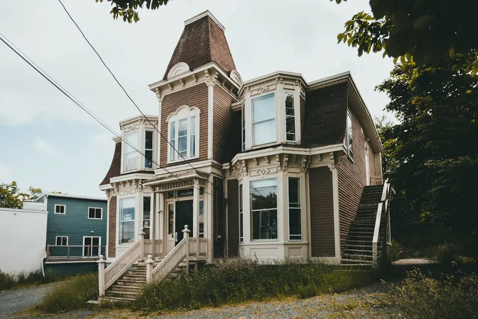 Elegant Victorian-style house featuring detailed architecture and wooden siding surrounded by lush trees.