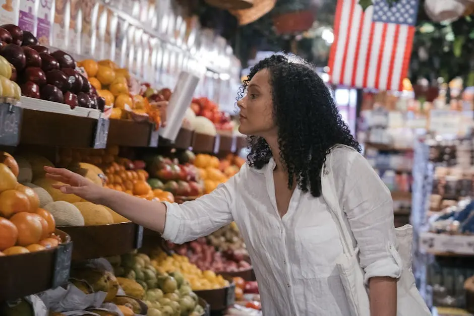 A woman selects fresh fruits in a grocery store with a variety of produce and an American flag in the background.