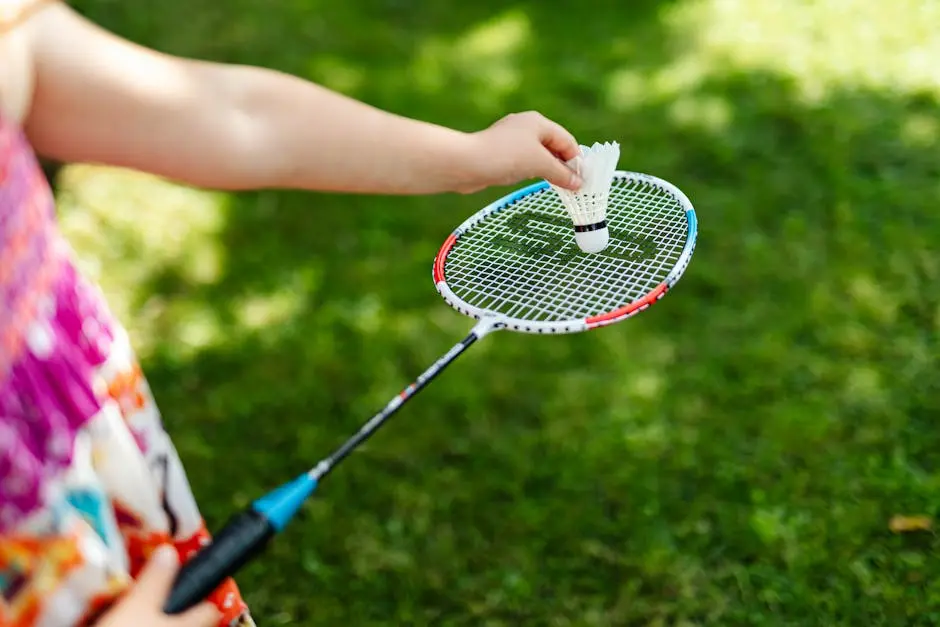 A detailed close-up of a person holding a badminton racket and shuttlecock outdoors.