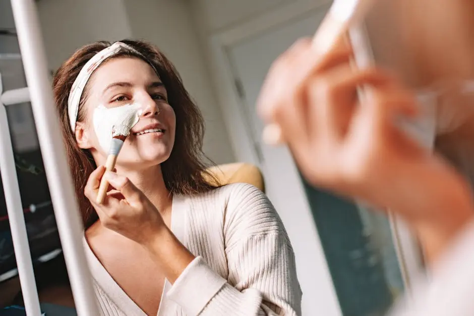 Woman enjoys a skincare routine, applying a facial mask with a brush in front of a mirror.