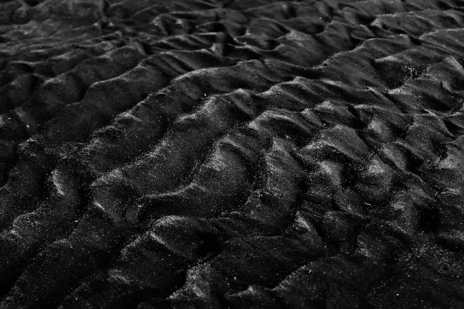 Close-up of textured black sand dunes in monochrome, showcasing natural patterns and textures.