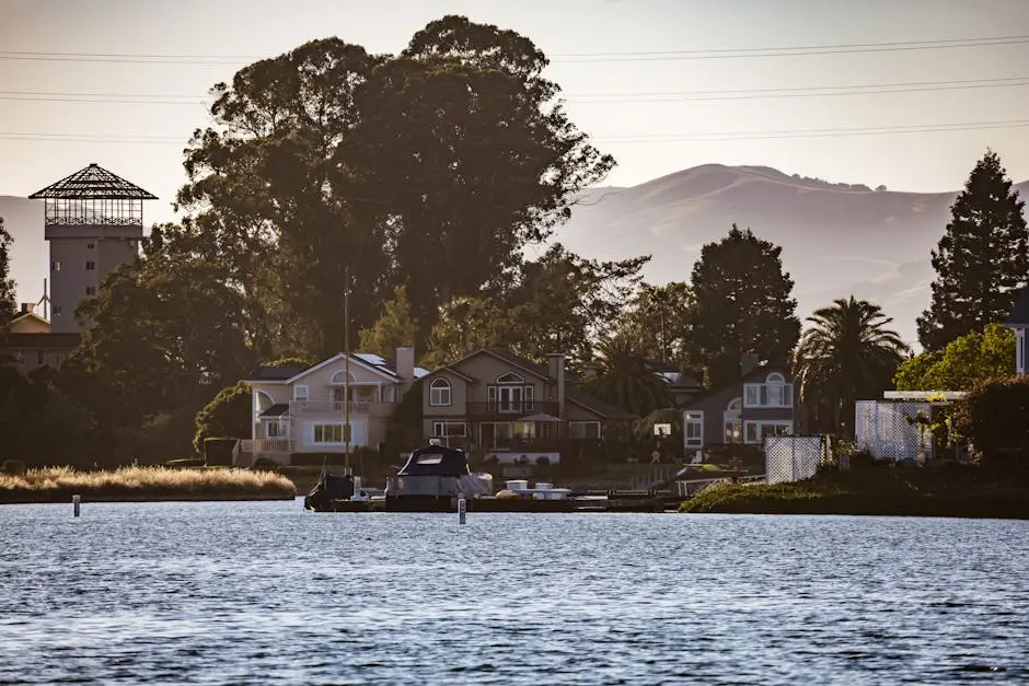Scenic view of waterfront homes with boat dock on a tranquil lake, surrounded by lush greenery and mountain backdrop.