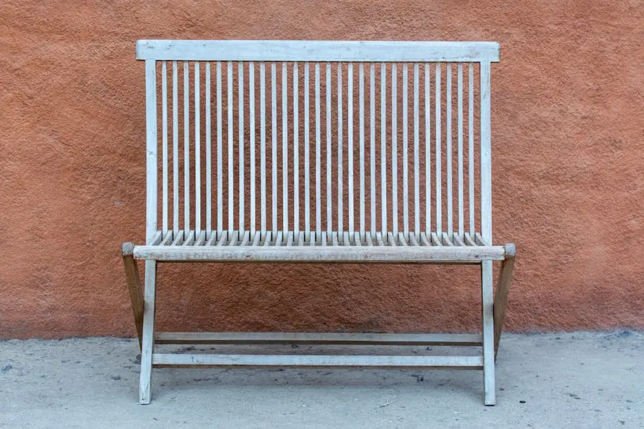 An antique wooden bench stands in front of a textured orange wall, showcasing rustic charm.