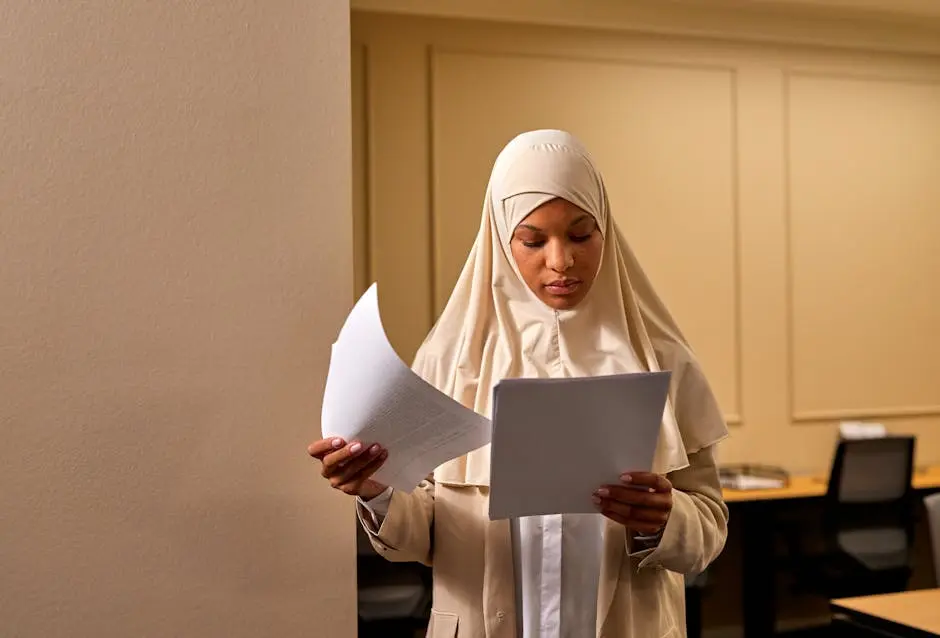 A professional woman in a hijab reviews documents in an office setting.