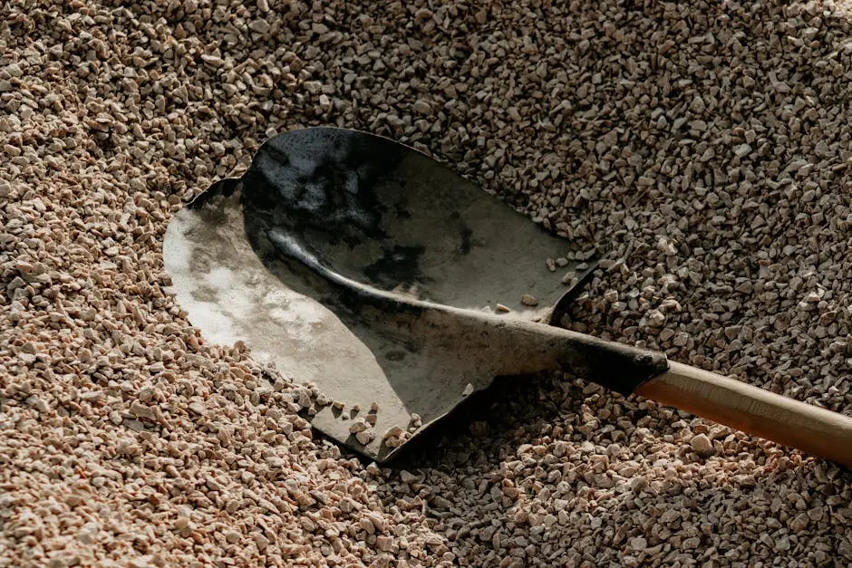 A metal shovel lying on a pile of small pebbles, suggesting outdoor landscaping or construction activities.