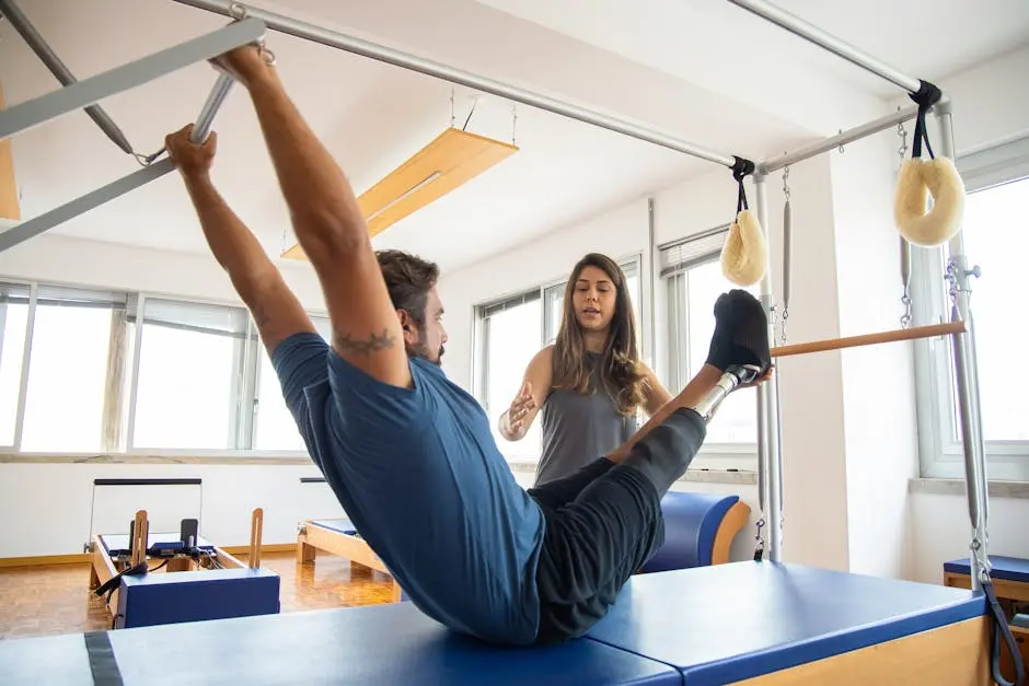 Man with prosthetic leg doing Pilates exercise under trainer’s guidance in a gym.