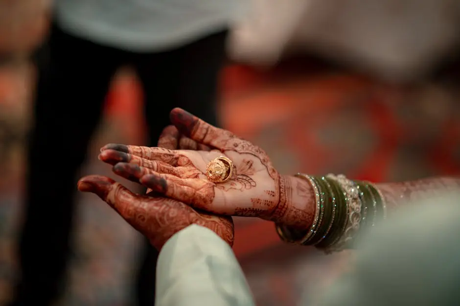 Close-up of hands with henna designs holding a golden ring, symbolizing love and commitment.