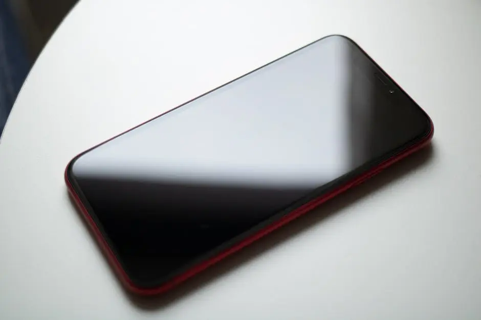 A sleek red smartphone placed on a white table showcasing modern digital technology.