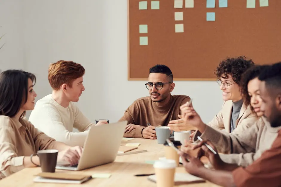 A diverse group of professionals engage in a collaborative meeting around a wooden table in an office environment.