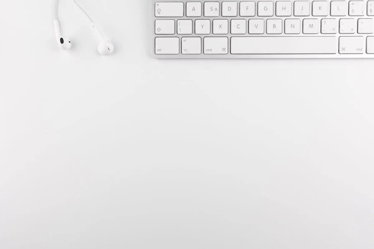 Top view of a white minimalist desk featuring a keyboard and earphones, ideal for technology themes.