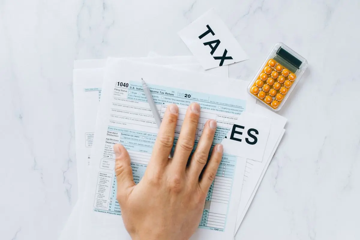 Close-up of a hand on tax form 1040 with a calculator on a desk.