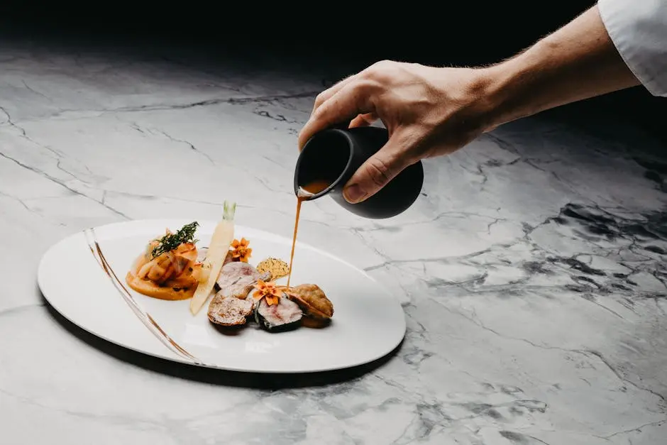 A hand pouring sauce over an elegantly presented gourmet dish on a marble surface, showcasing refined culinary art.