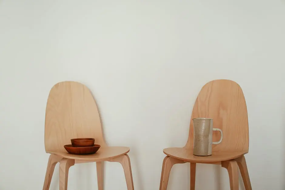 Two minimalist wooden chairs with a ceramic mug and bowls create a calm, modern aesthetic.