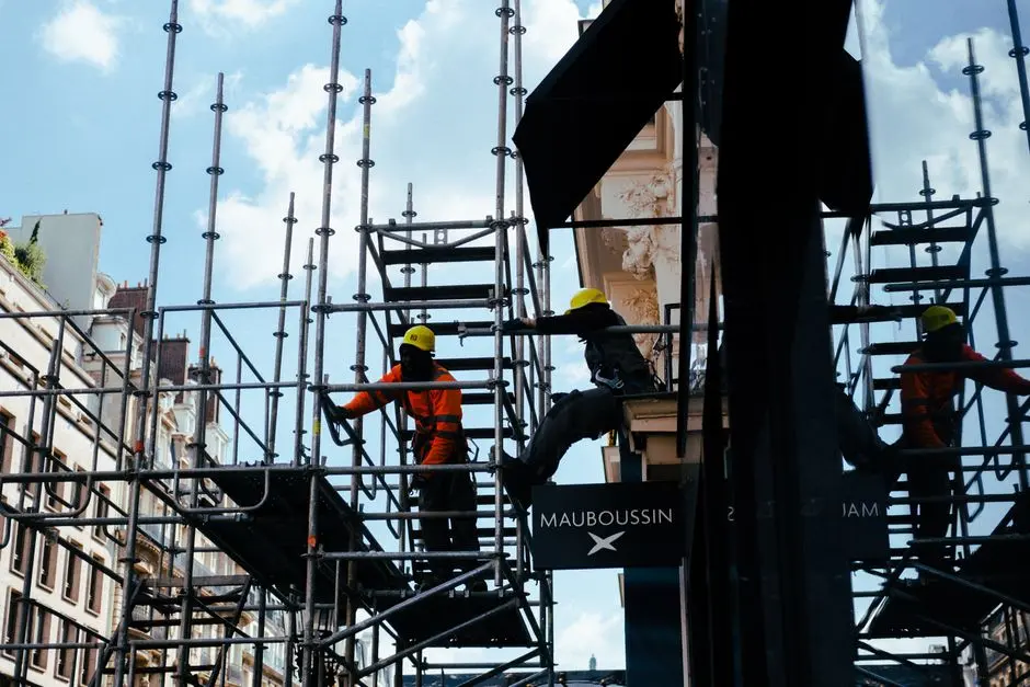 Silhouetted construction workers on scaffolding in an urban environment under blue skies.