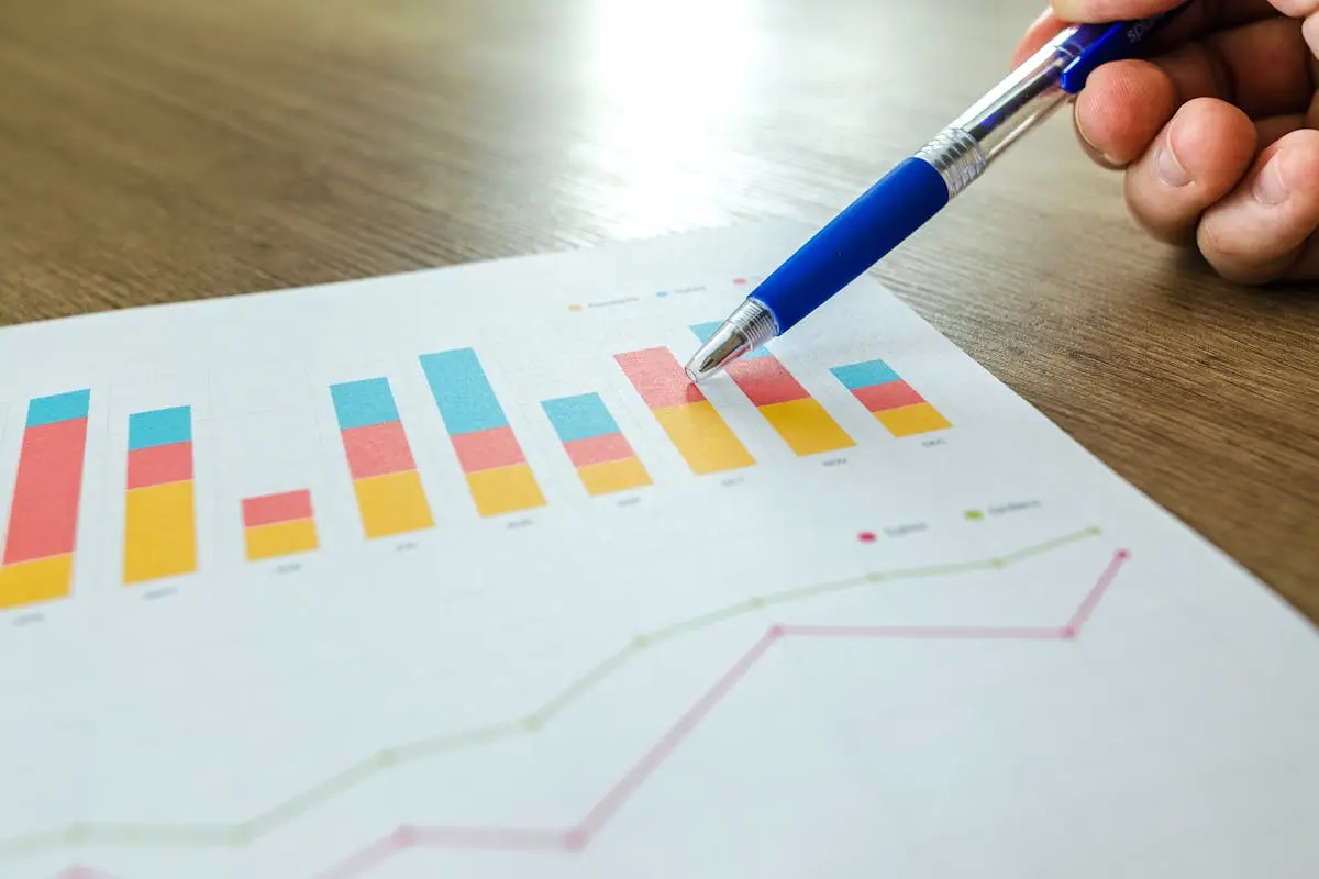 Detailed close-up of a fractional cfo firms pointing at colorful charts with a blue pen on wooden surface.
