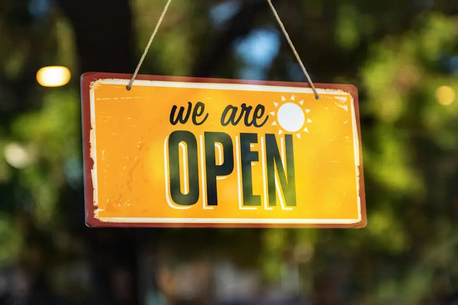 Bright yellow 'We Are Open' sign hanging on a glass door with reflections.
