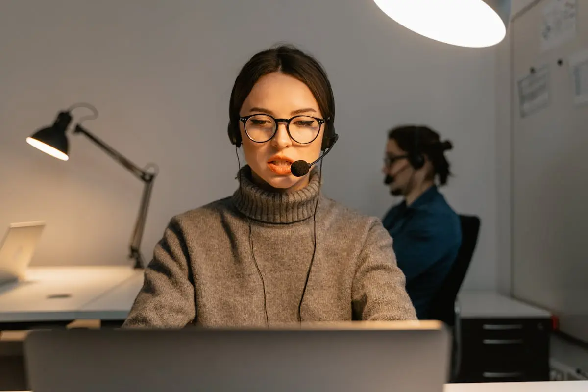 Focused call center agent wearing glasses and headset at work indoors.