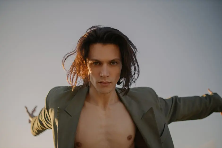 A young man poses confidently outdoors wearing a stylish jacket with an open shirt. Dramatic lighting enhances the scene.