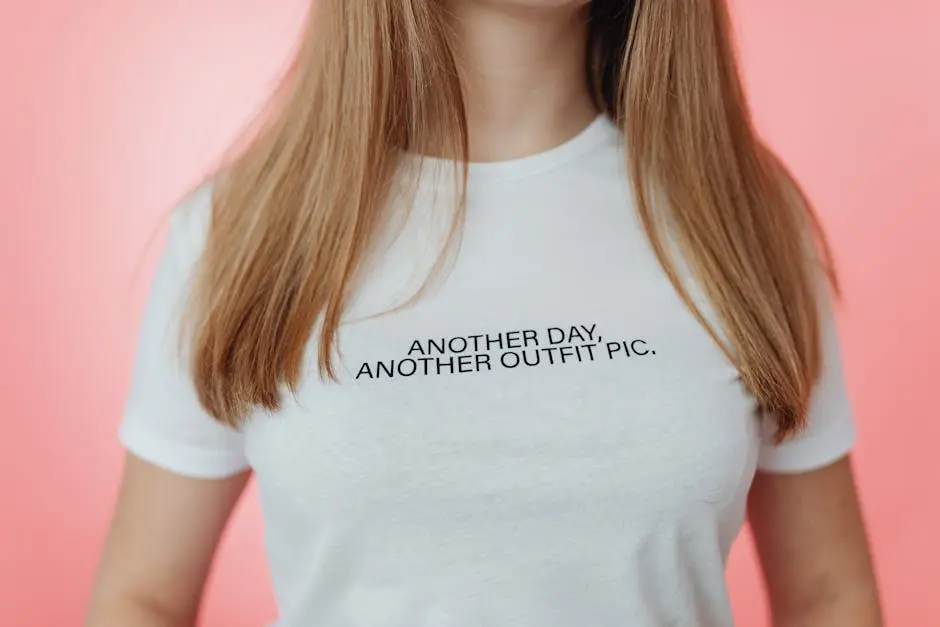 Close-up of a t-shirt with the slogan ‘ANOTHER DAY, ANOTHER OUTFIT PIC’ against a pink background.
