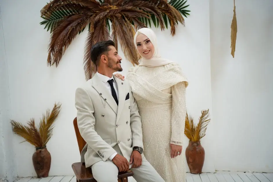 Stylish couple in wedding attire posing elegantly with tropical palm decor in a modern indoor setting.
