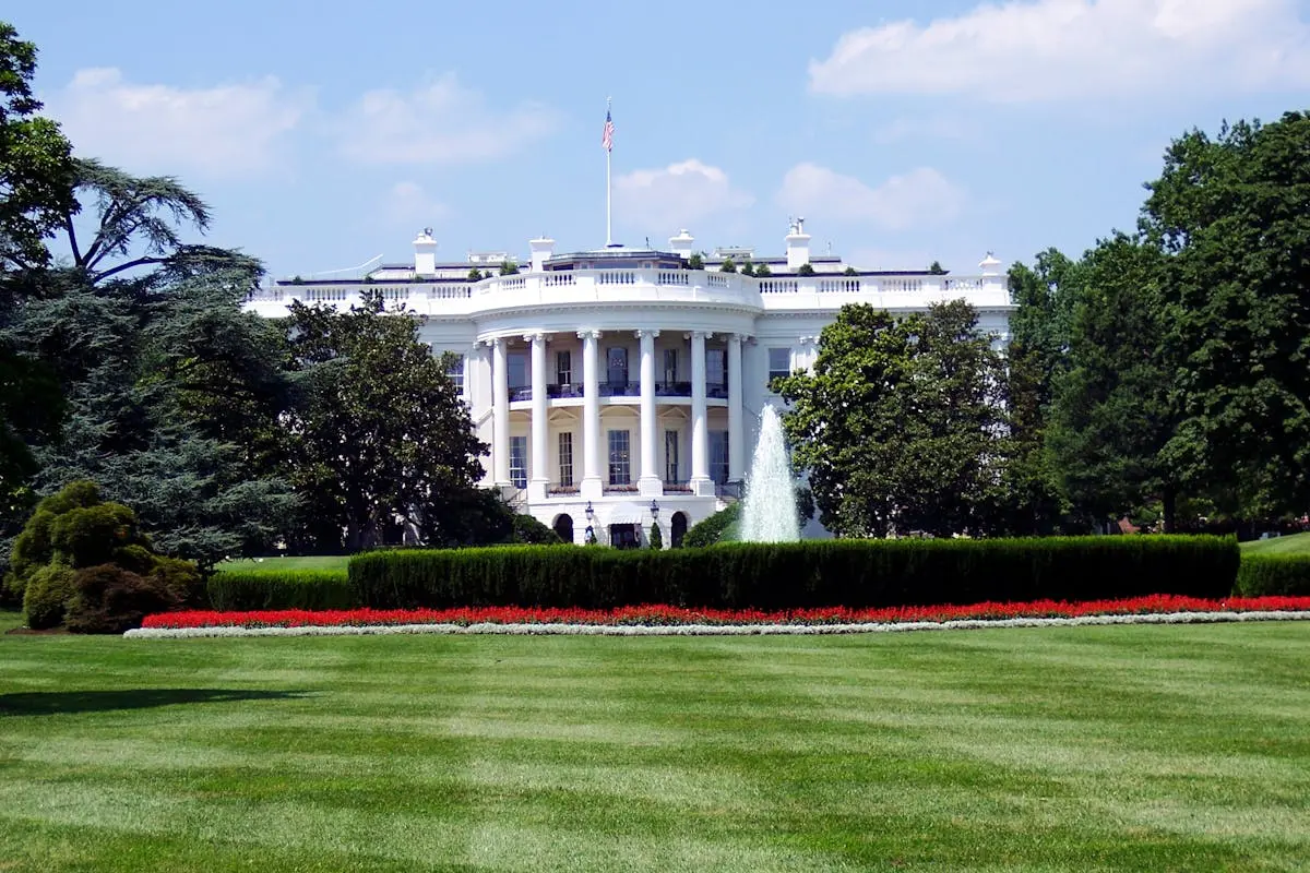 Iconic view of the White House with lush gardens and a central fountain on a sunny day.