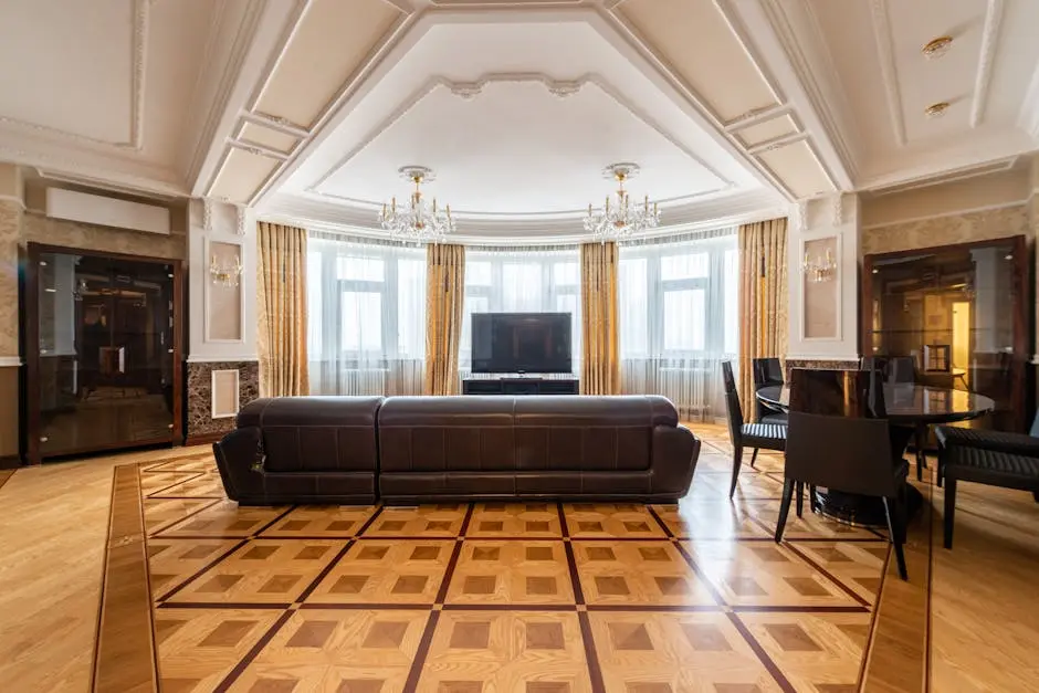 Spacious living room with a leather couch, large TV, and elegant decor, featuring chandeliers and parquet flooring.
