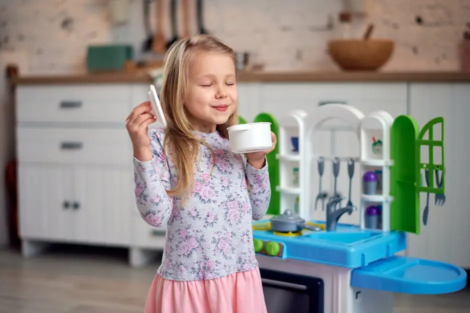 Happy child with blonde hair playing with a toy kitchen and enjoying a pretend tea party.