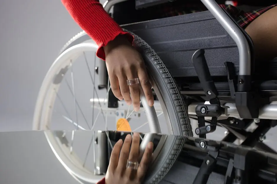 Close-up of a person’s hand on a wheelchair wheel, reflected in glass, highlighting mobility and disability themes.