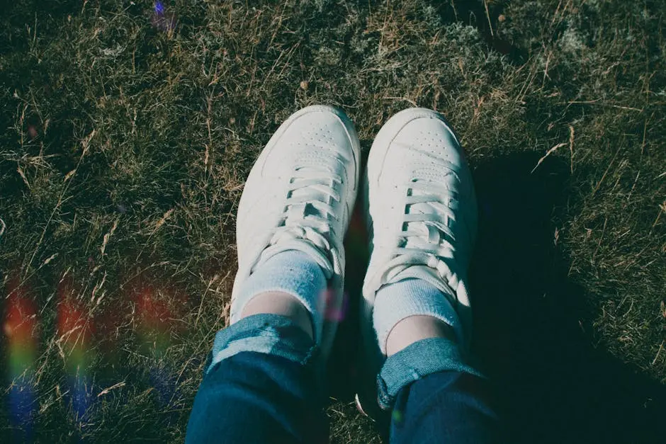 Top view of white sneakers and jeans on grassy field, natural sunlight.