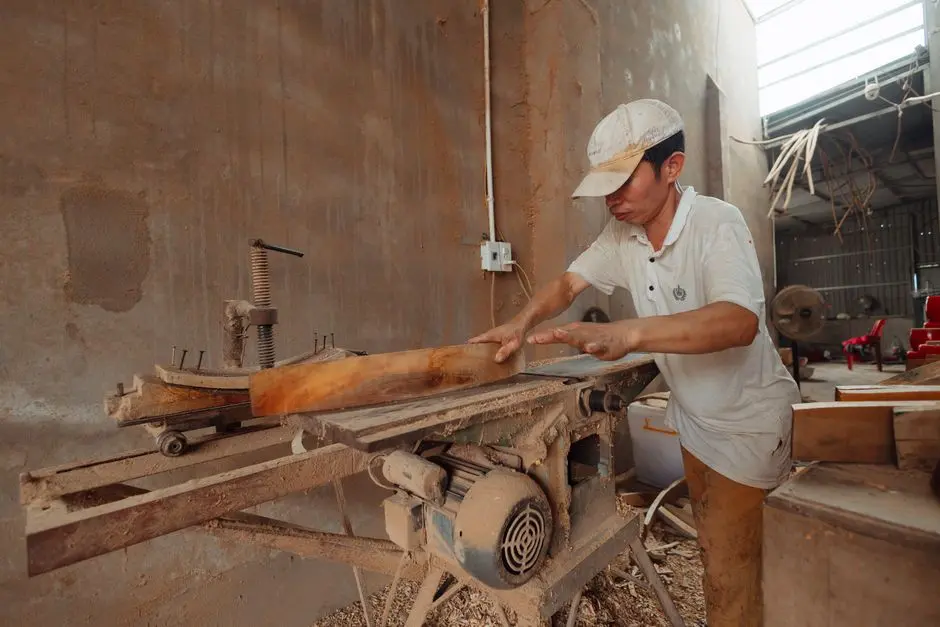 A carpenter in a dusty workshop precisely cuts wood using an industrial saw.