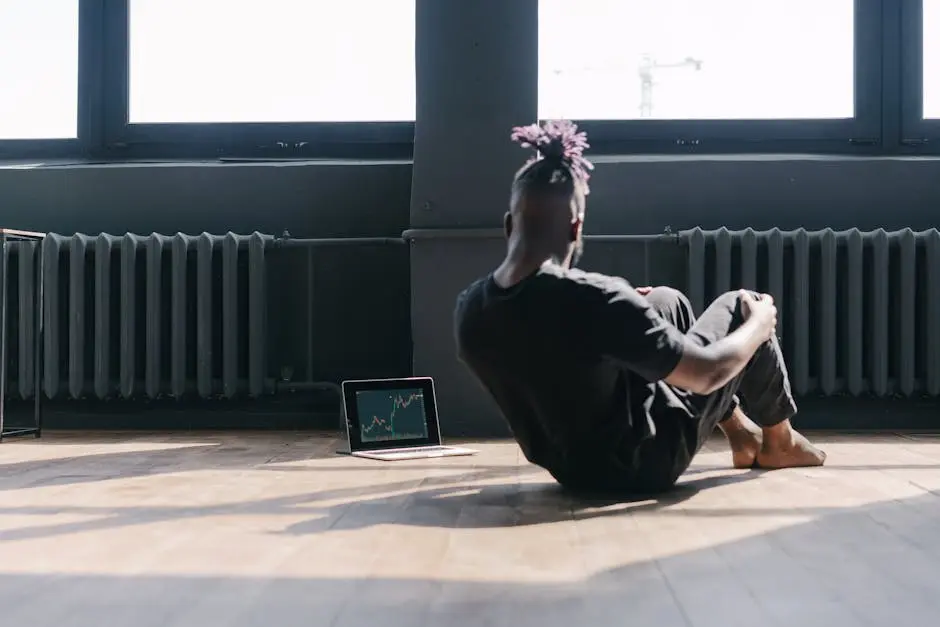 Man doing sit-ups near a laptop showing stock market trends in a bright room.