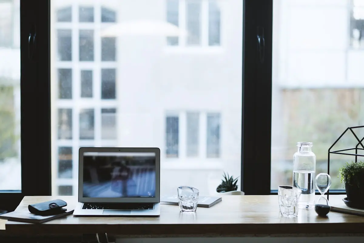 Sleek office desk setup featuring a laptop, glass of water, and open window view.