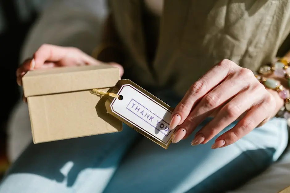 Close-up of hands holding a gift box with a Thank You tag attached, in natural lighting.