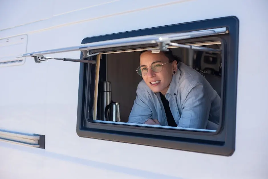 A woman with eyeglasses looks out the window of an RV parked in Portugal on a sunny day.